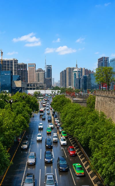 Xi'an ancient city wall with its tower and red lanterns beside a tree-lined avenue and the modern skyline behind