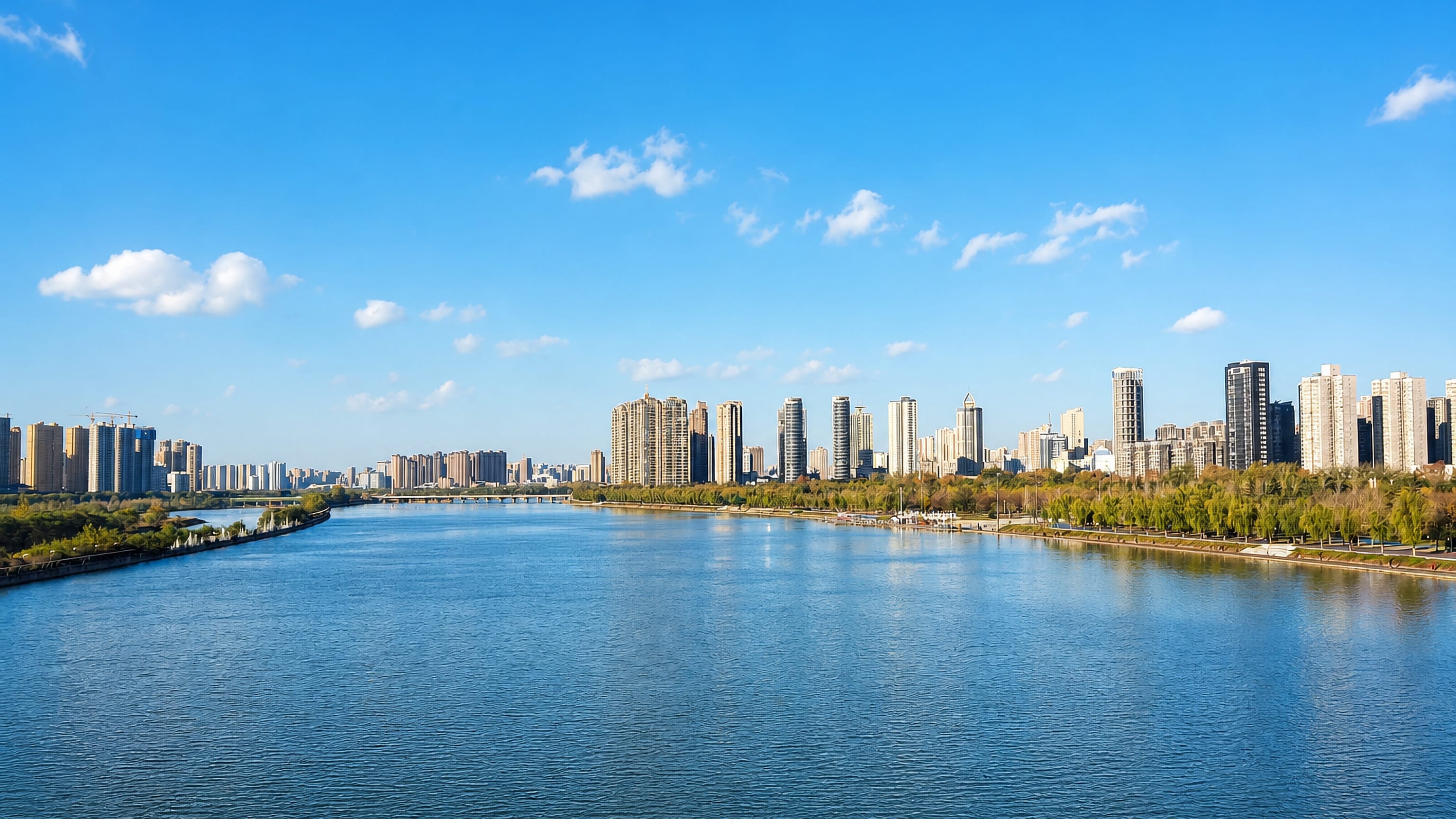 The Wei River curving past Xianyang's riverside high-rise skyline and tree-lined embankment under a clear blue sky
