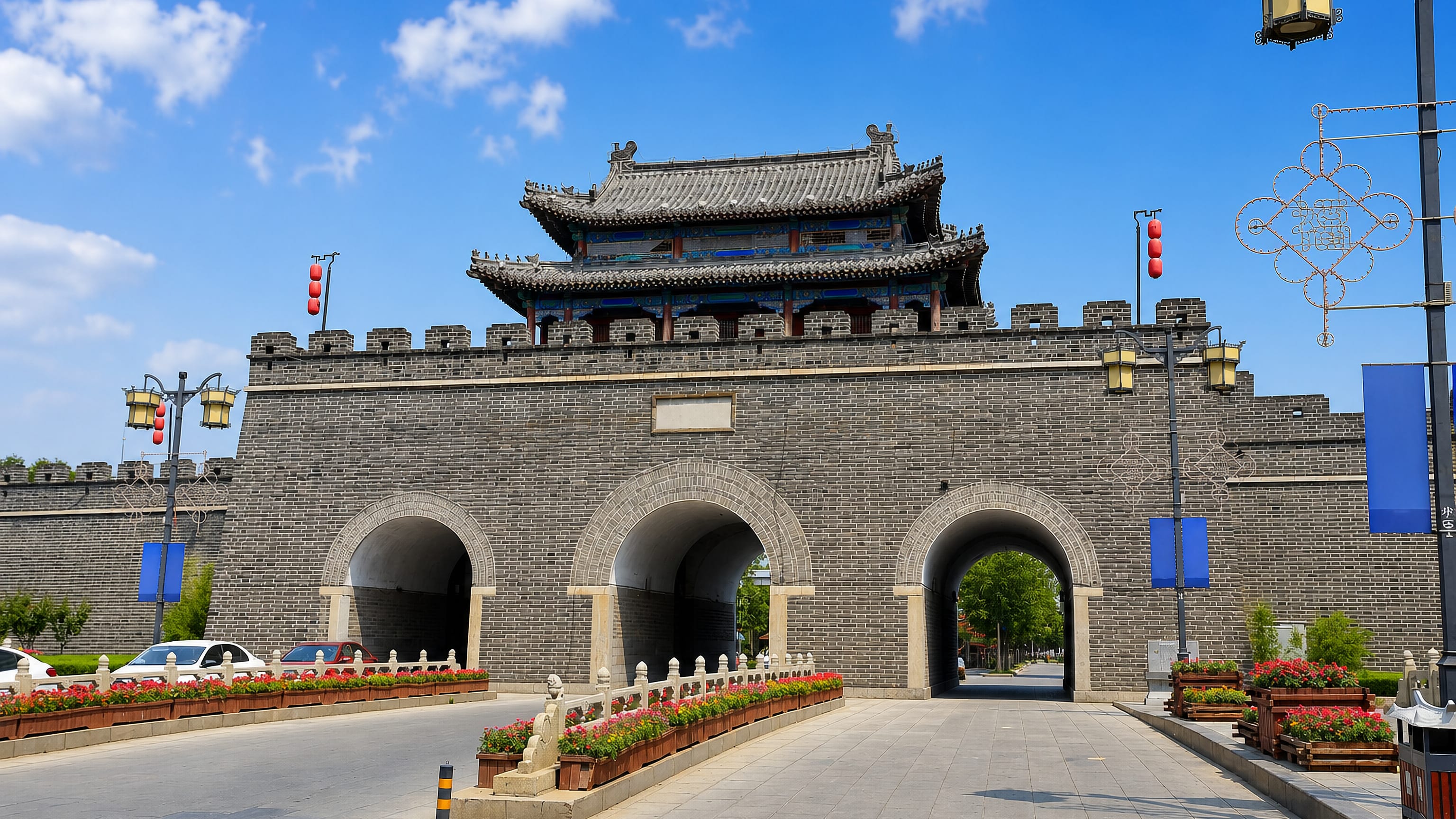 Qufu's restored Ming-dynasty city wall gate and tower, red lanterns and flowerbeds along the approach.