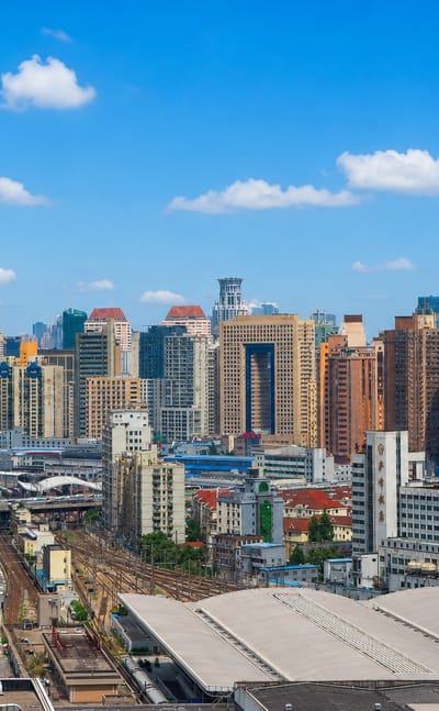 Jing'an rooftops with the Shanghai Tower and World Financial Center rising on the skyline beyond rail lines.