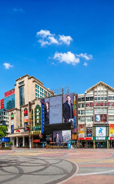 Pedestrian shopping plaza on Nanjing Road, Shanghai, lined with billboard-covered storefronts and decorative paving under a blue sky
