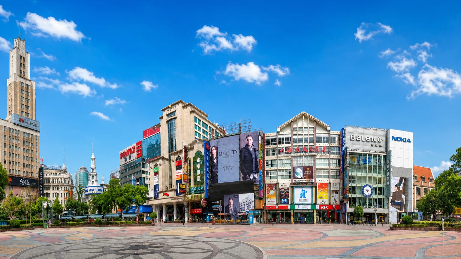Pedestrian shopping plaza on Nanjing Road, Shanghai, lined with billboard-covered storefronts and decorative paving under a blue sky