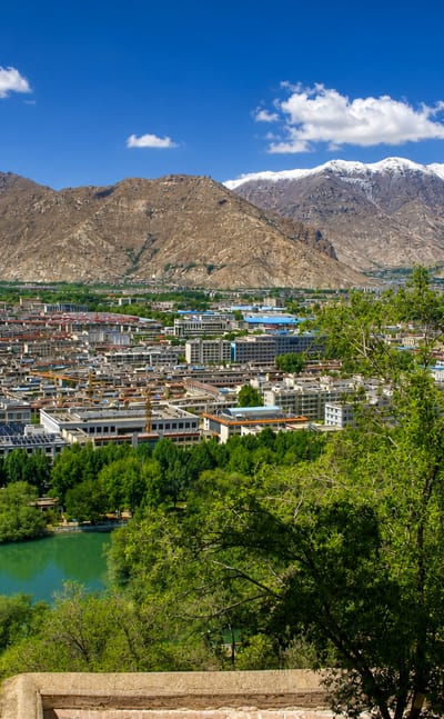 Lhasa, Tibet, spread across a valley beneath arid snow-capped mountains, with a green pond in the foreground.