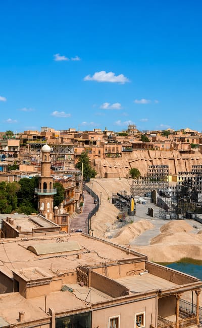 Earthen Old Town buildings and a minaret in Kashgar with modern towers rising beyond under a clear blue sky.