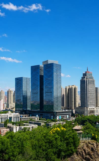 Ürümqi's high-rise downtown with a spire-topped tower and the Tian Shan mountains behind a green ridge.
