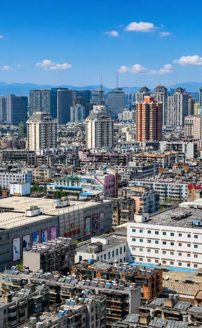 Dense rooftops and high-rises of Kunming stretching toward mountains under a blue sky.