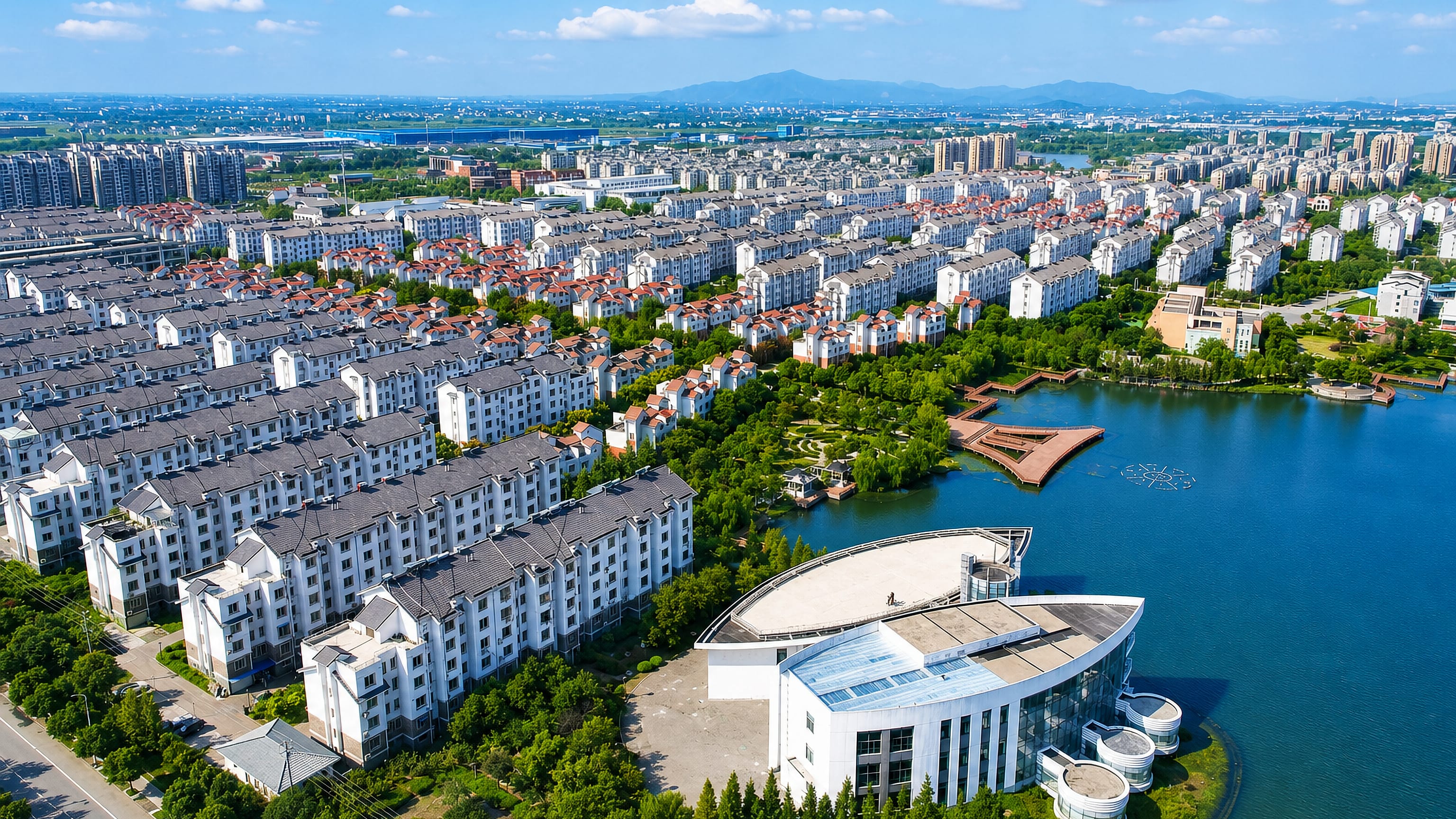 Aerial view of Huzhou, Zhejiang, China, with white apartment rows and a modern lakeside building.