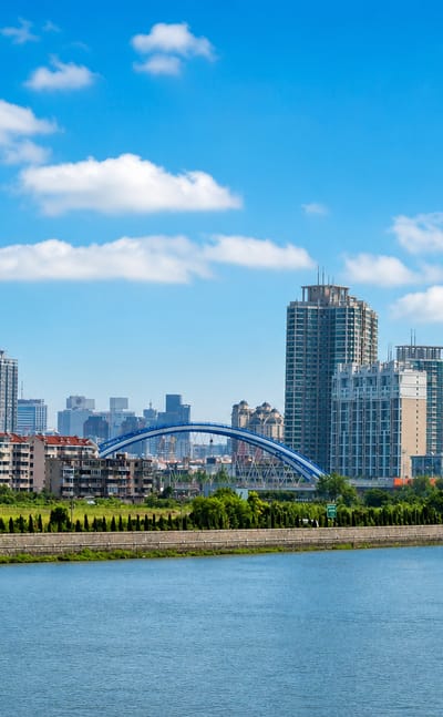 Residential towers and an arched blue bridge along a river in Ningbo under a bright blue sky.