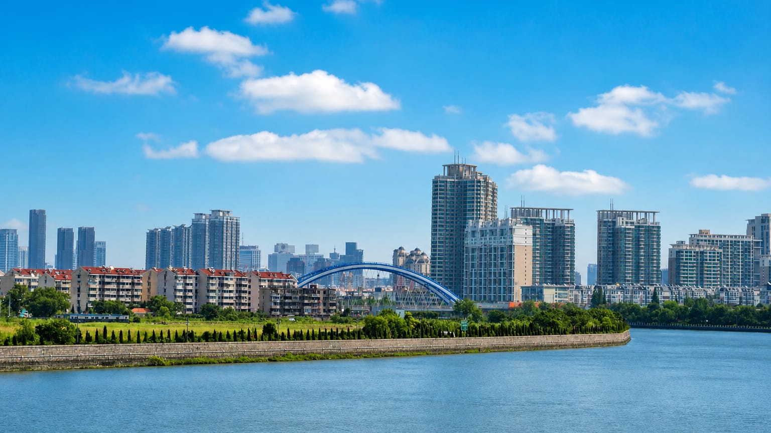 Residential towers and an arched blue bridge along a river in Ningbo under a bright blue sky.
