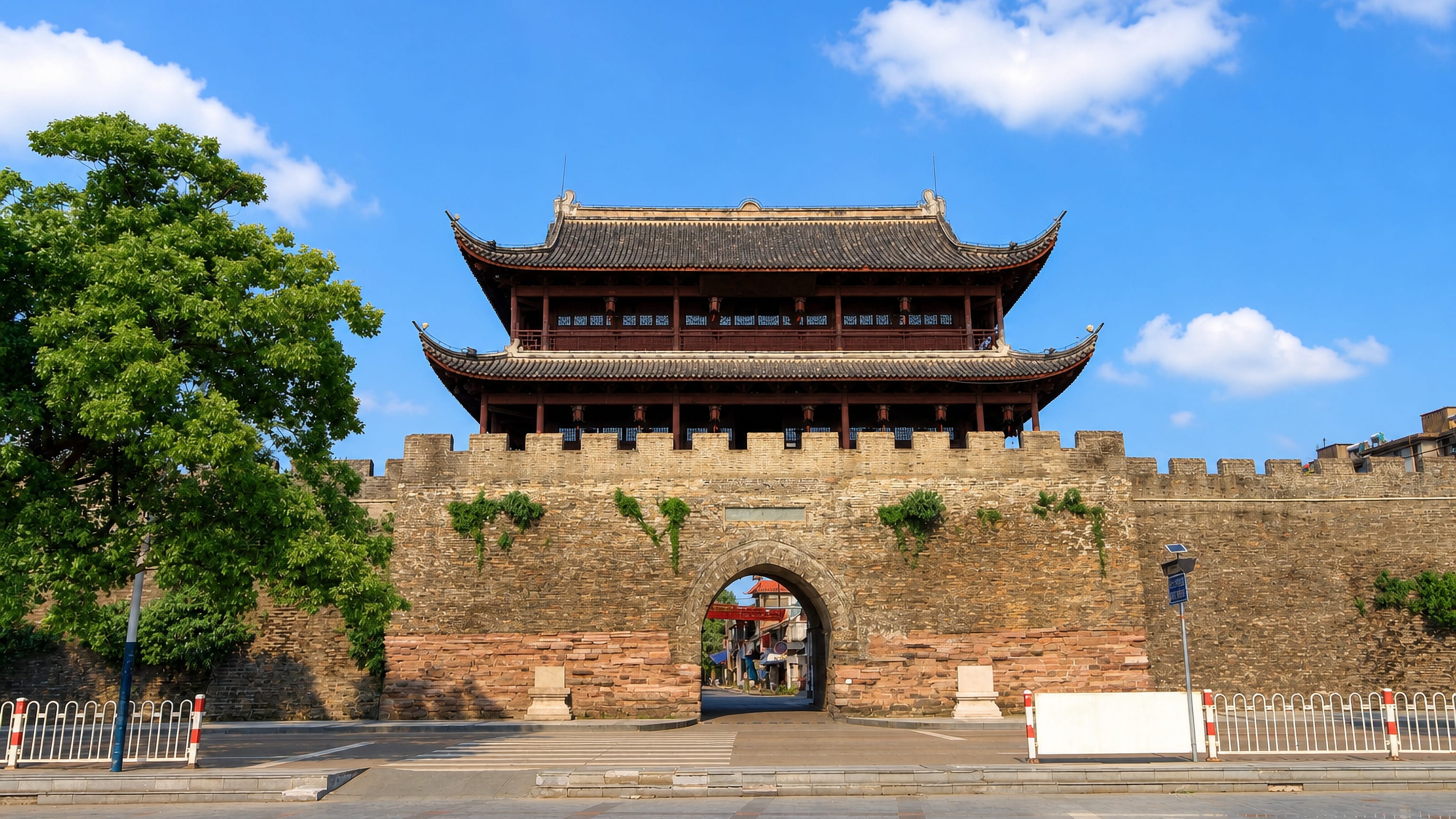 Restored stone city gate and battlemented wall topped by a tiered timber pavilion in Quzhou, China.
