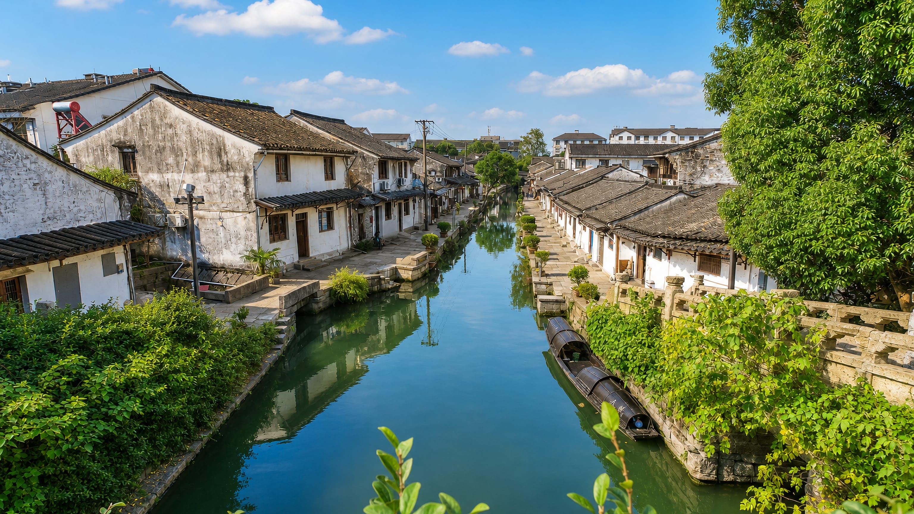 A canal in Shaoxing lined with white-walled, black-tiled Jiangnan houses, with a black-awning boat moored alongside.