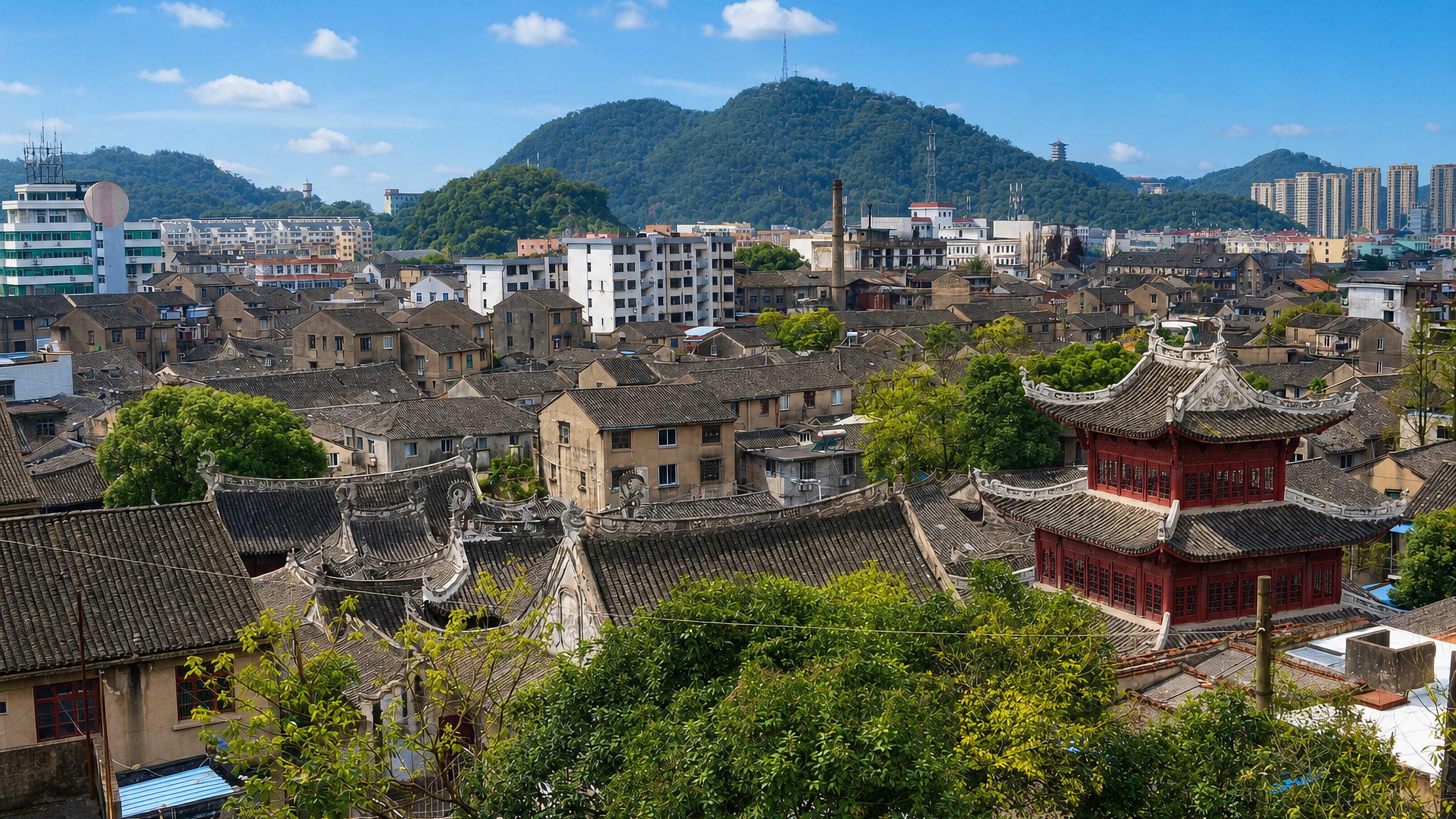 Tiled rooftops and a red pavilion in Taizhou's Jiaojiang district, with wooded hills and towers behind.