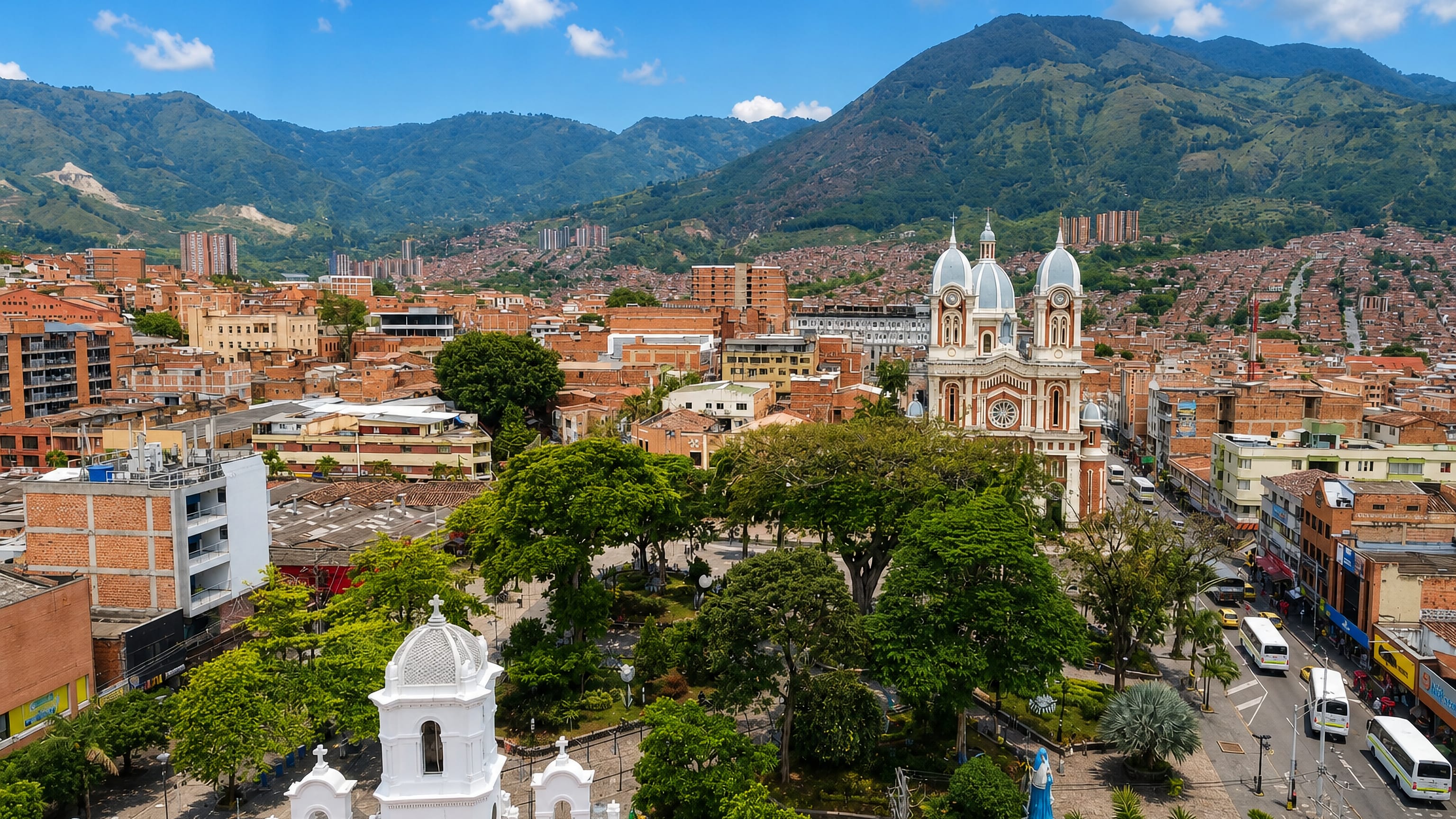 Aerial view of Bello's tree-filled central park and twin-towered church below the green slopes of the Aburra Valley.