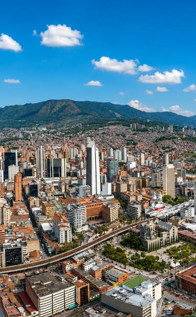 Aerial view of downtown Medellín high-rises ringed by the green Aburrá Valley mountains under a blue sky