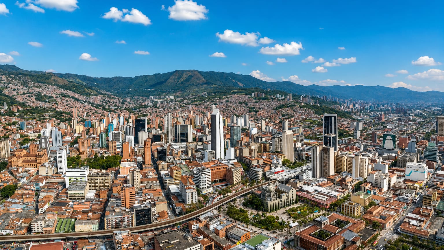 Aerial view of downtown Medellín high-rises ringed by the green Aburrá Valley mountains under a blue sky