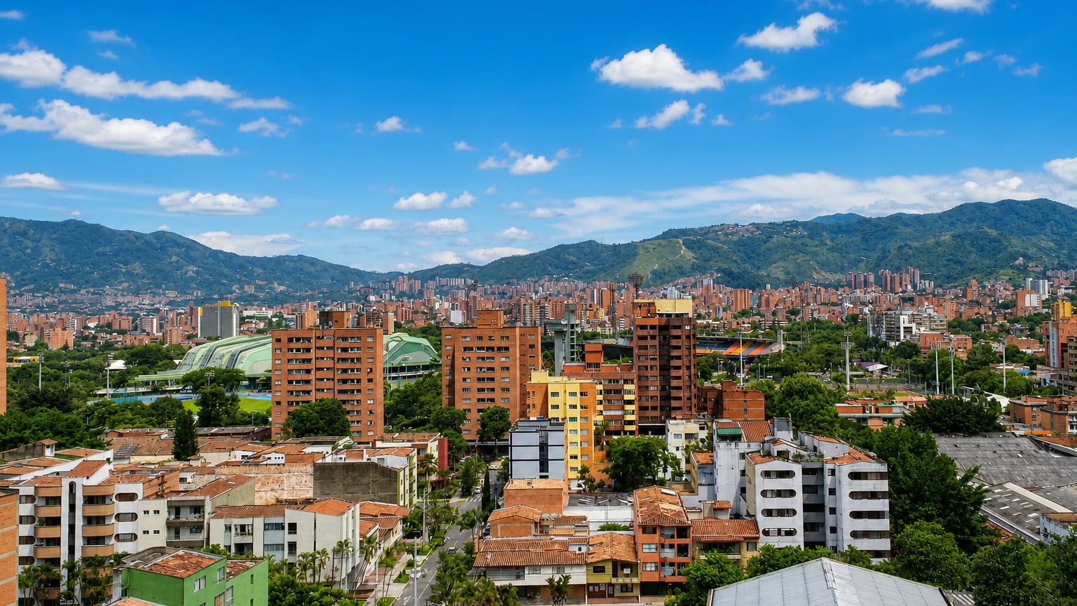Dense red-brick mid-rises and a stadium complex fill the Aburra Valley below Andean peaks in Medellin's Laureles-Estadio district.