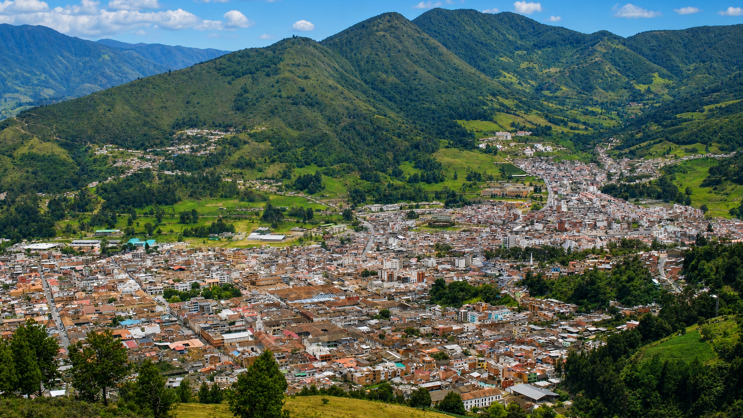 Pamplona, Colombia, spread across a green Andean valley ringed by forested mountains under a blue sky.