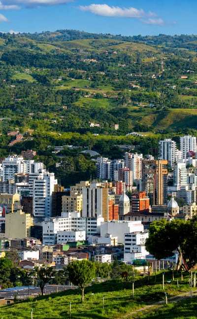 Aerial view of Pereira, Colombia, with high-rise buildings amid the green hills of the coffee region under blue sky.