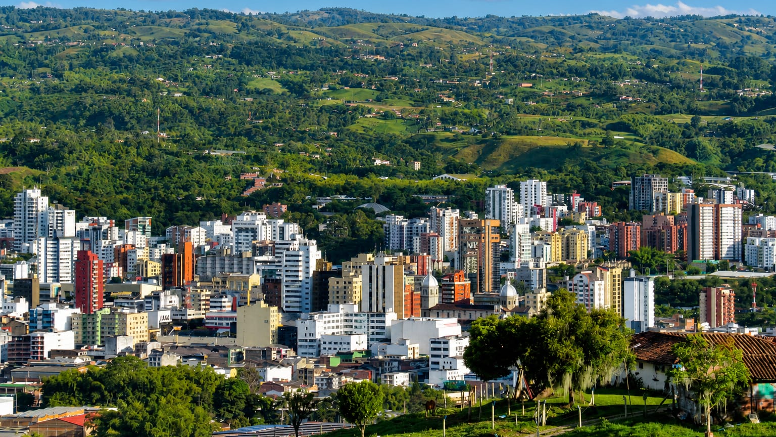 Aerial view of Pereira, Colombia, with high-rise buildings amid the green hills of the coffee region under blue sky.