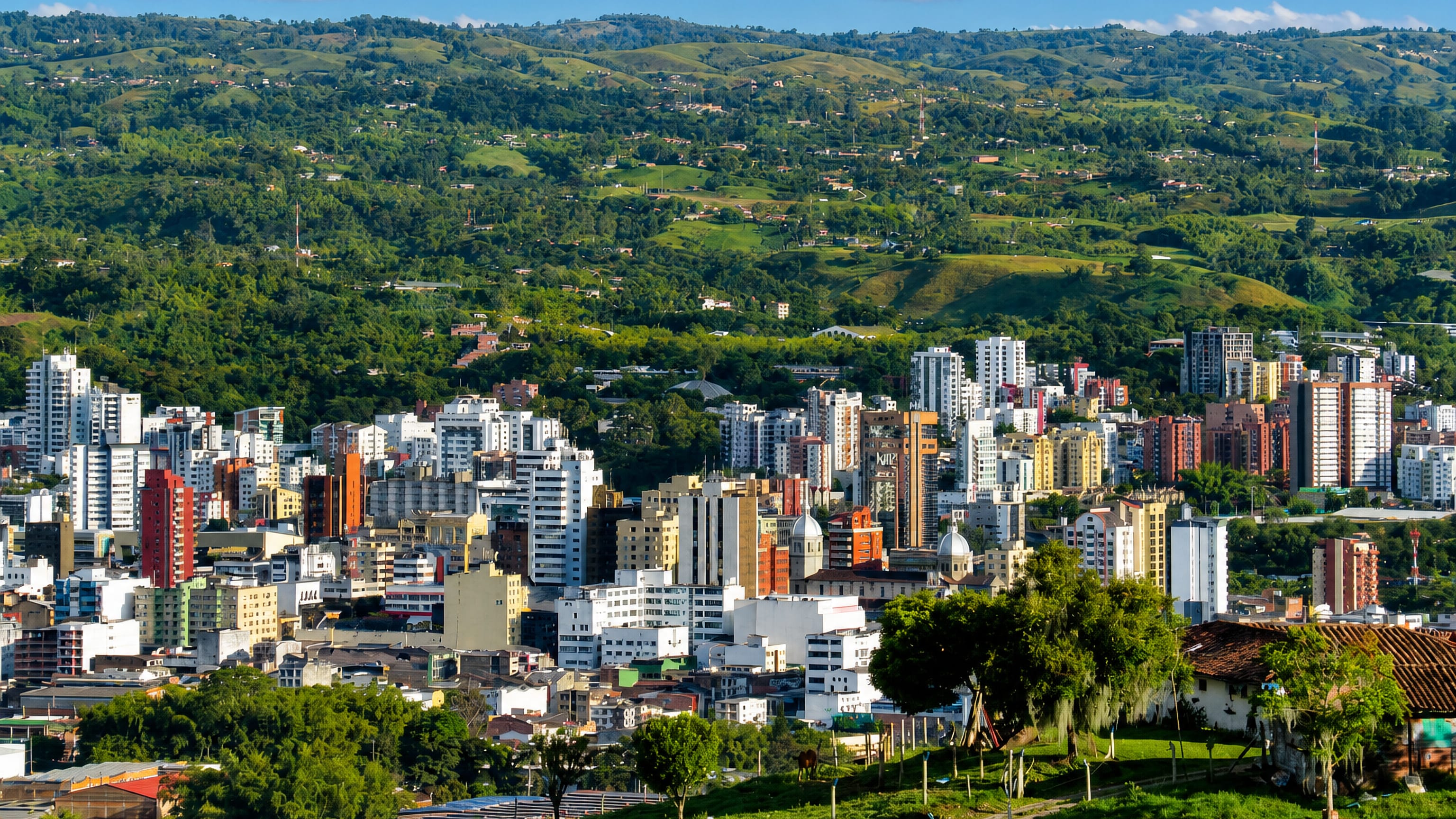 Aerial view of Pereira, Colombia, with high-rise buildings amid the green hills of the coffee region under blue sky.