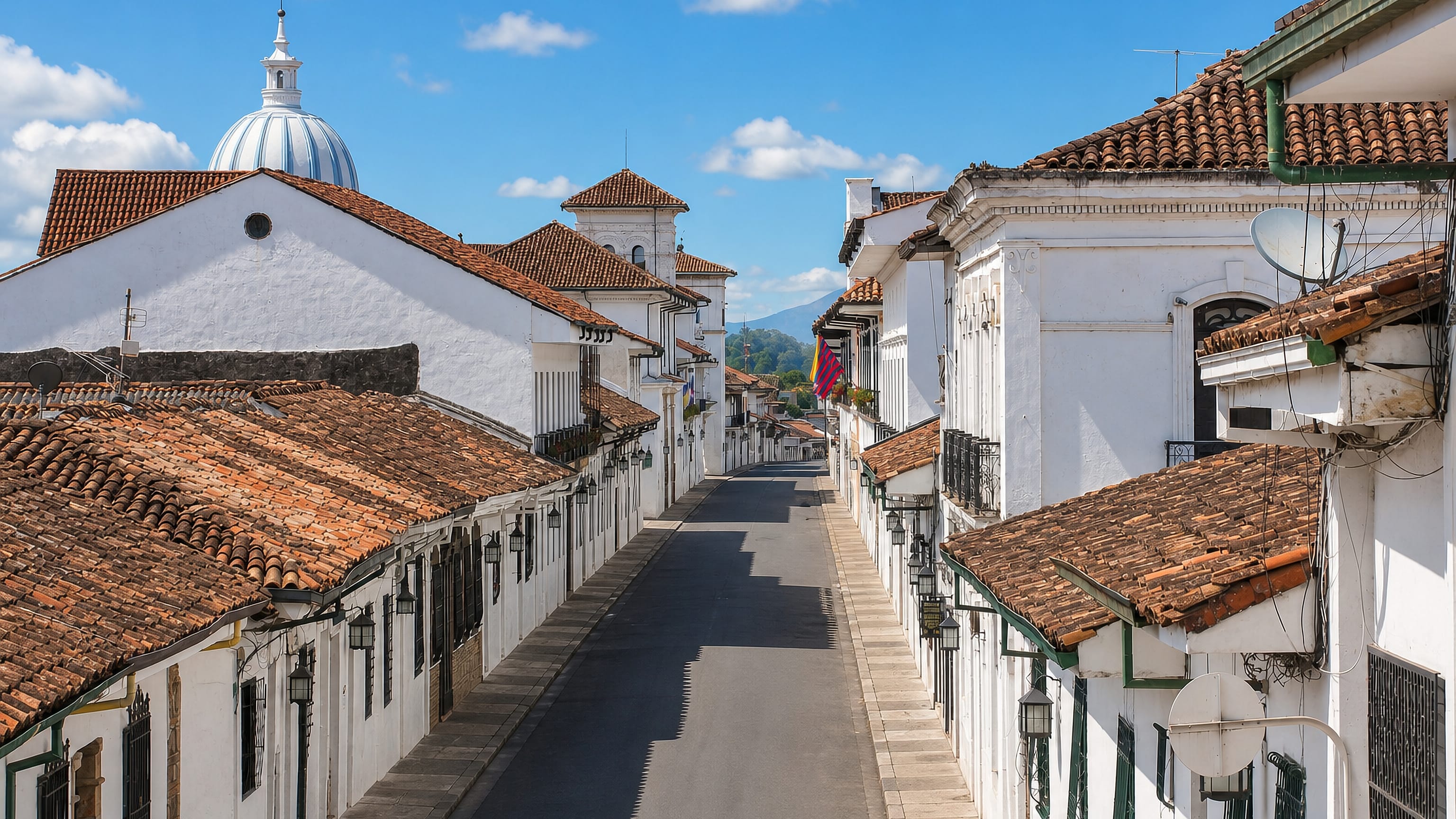 Whitewashed colonial houses with terracotta roofs and a church dome along a narrow street in Popayan.