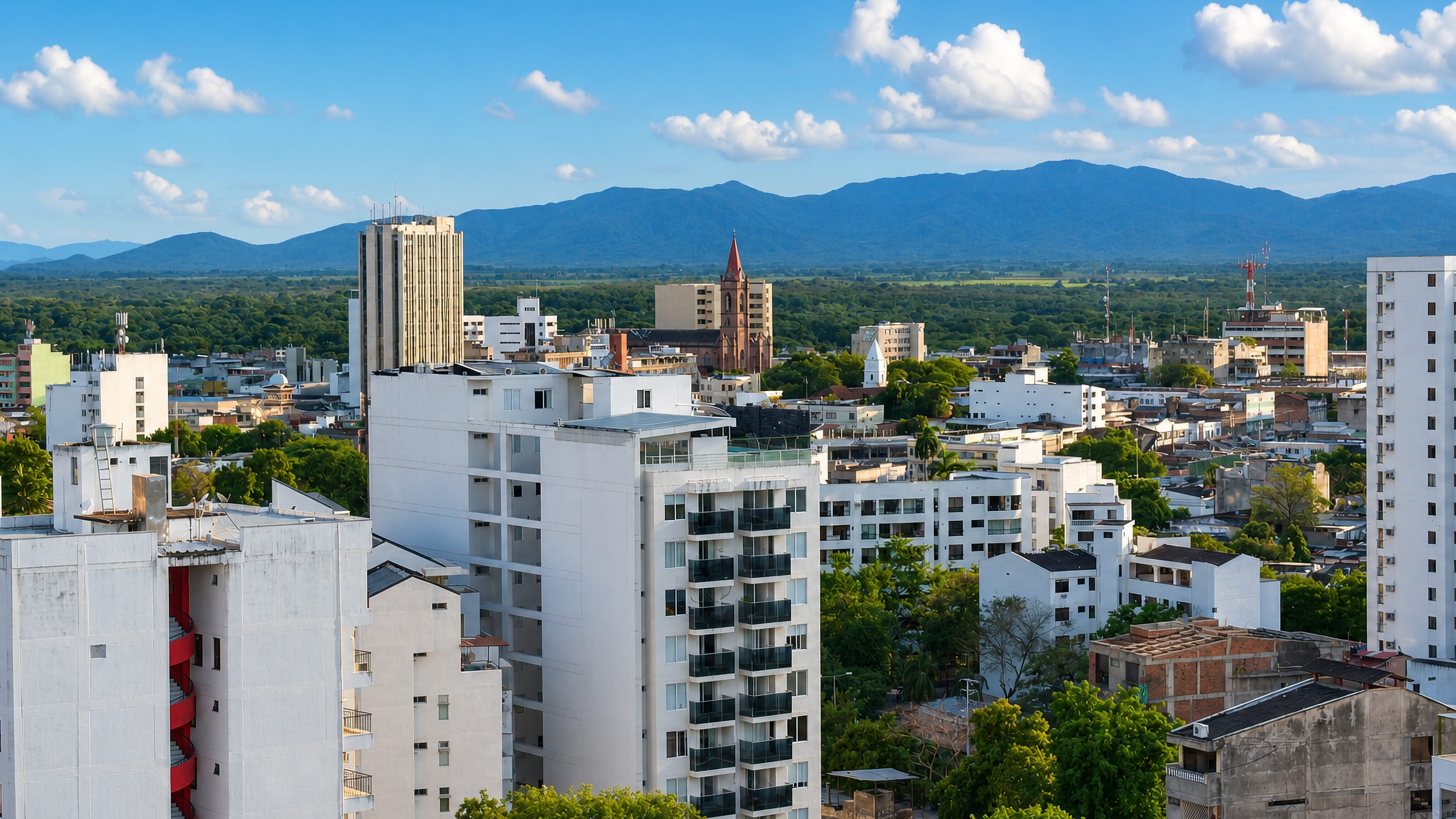 White apartment towers and a brick church spire in Neiva, Colombia, below the green Andean foothills.