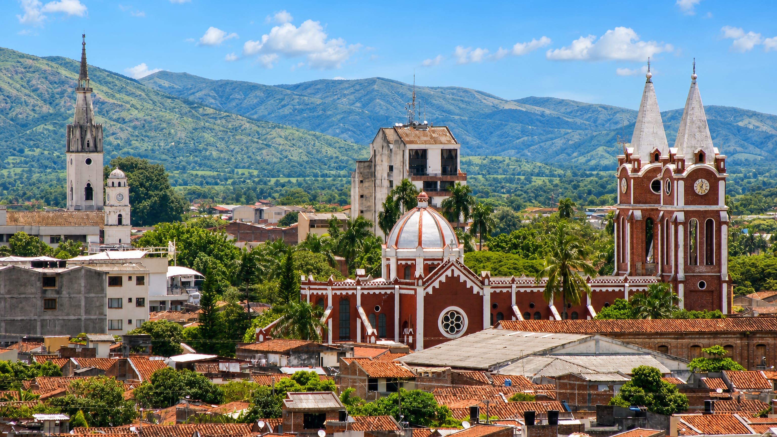 Red-tile rooftops and brick church towers in Tulua, Colombia, below green Andean foothills.