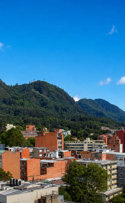 Brick rooftops of Chapinero backed by the green Eastern Hills of Bogota under a bright blue sky