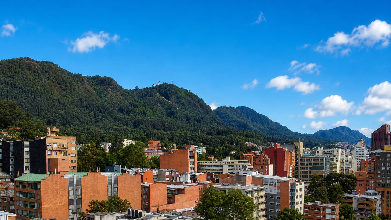 Brick rooftops of Chapinero backed by the green Eastern Hills of Bogota under a bright blue sky