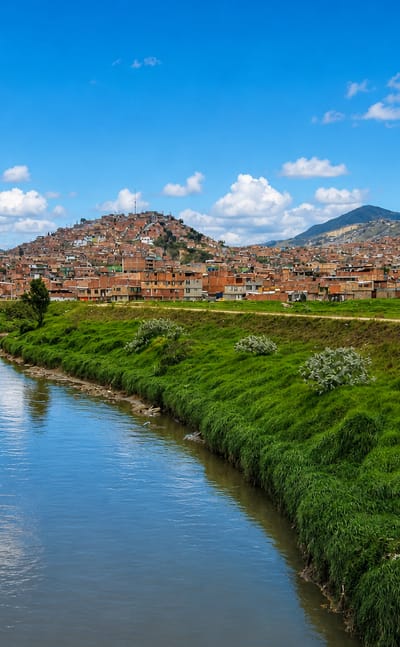 A canal winding past brick houses climbing the hillsides of the Ciudad Bolivar locality in southern Bogota