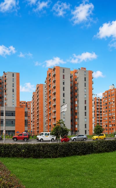 Rows of red-brick apartment towers along a landscaped boulevard in the Suba locality of Bogota under a blue sky