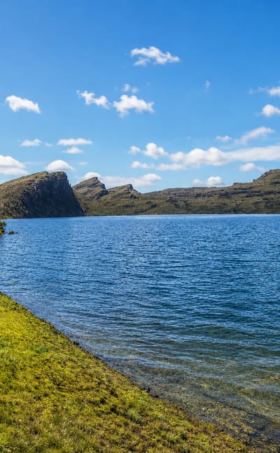 A high-altitude paramo lake ringed by grassy moorland hills in the rural Sumapaz locality of Bogota