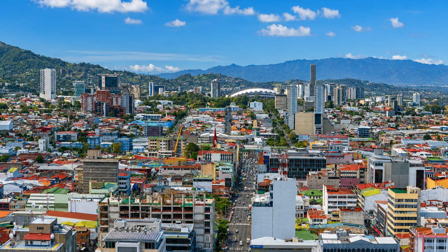 Aerial view of San José, Costa Rica, colorful rooftops filling a mountain-ringed valley with the national stadium.