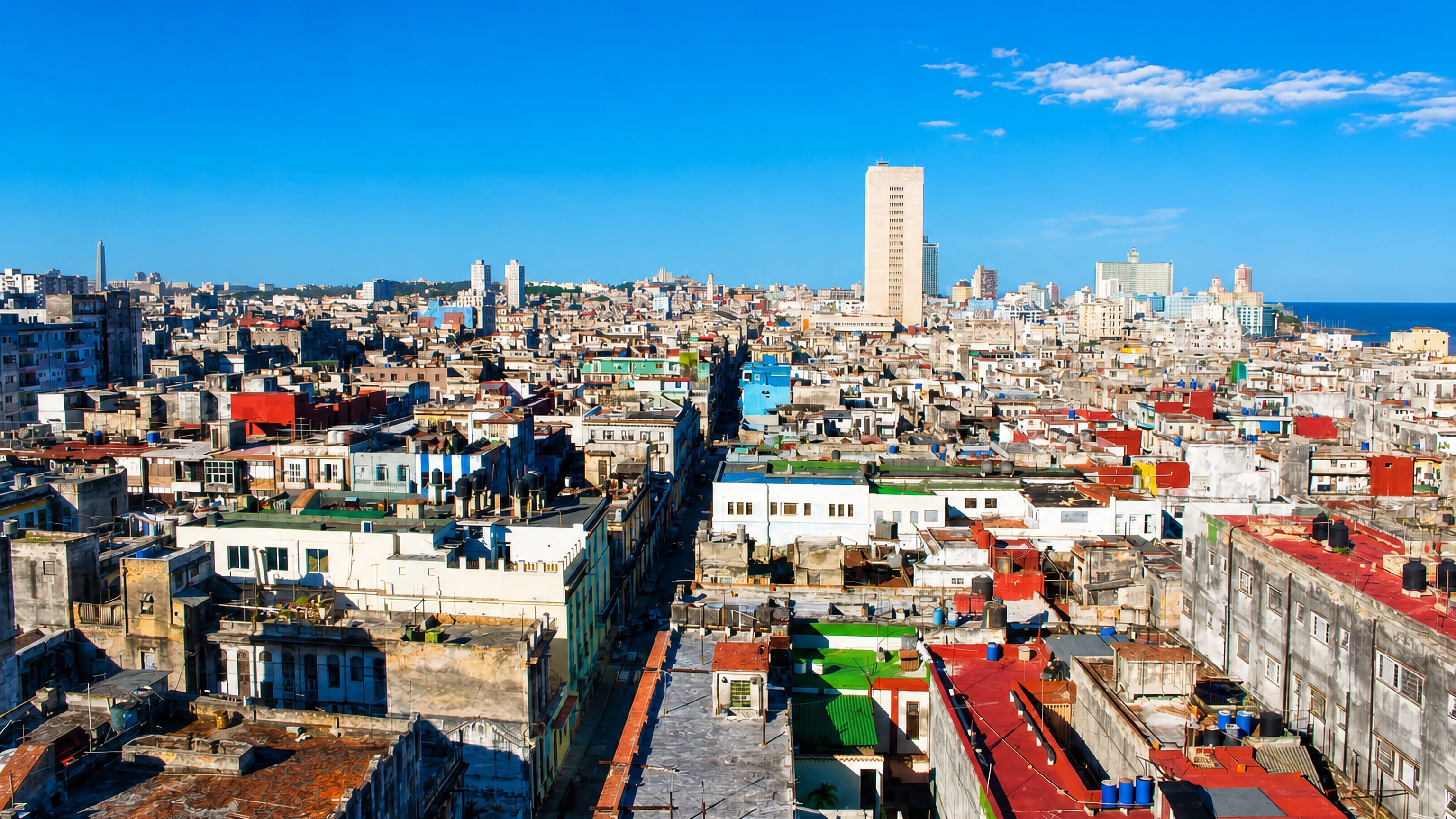 Dense colourful rooftops of Centro Habana stretching toward the sea under a clear blue Cuban sky.