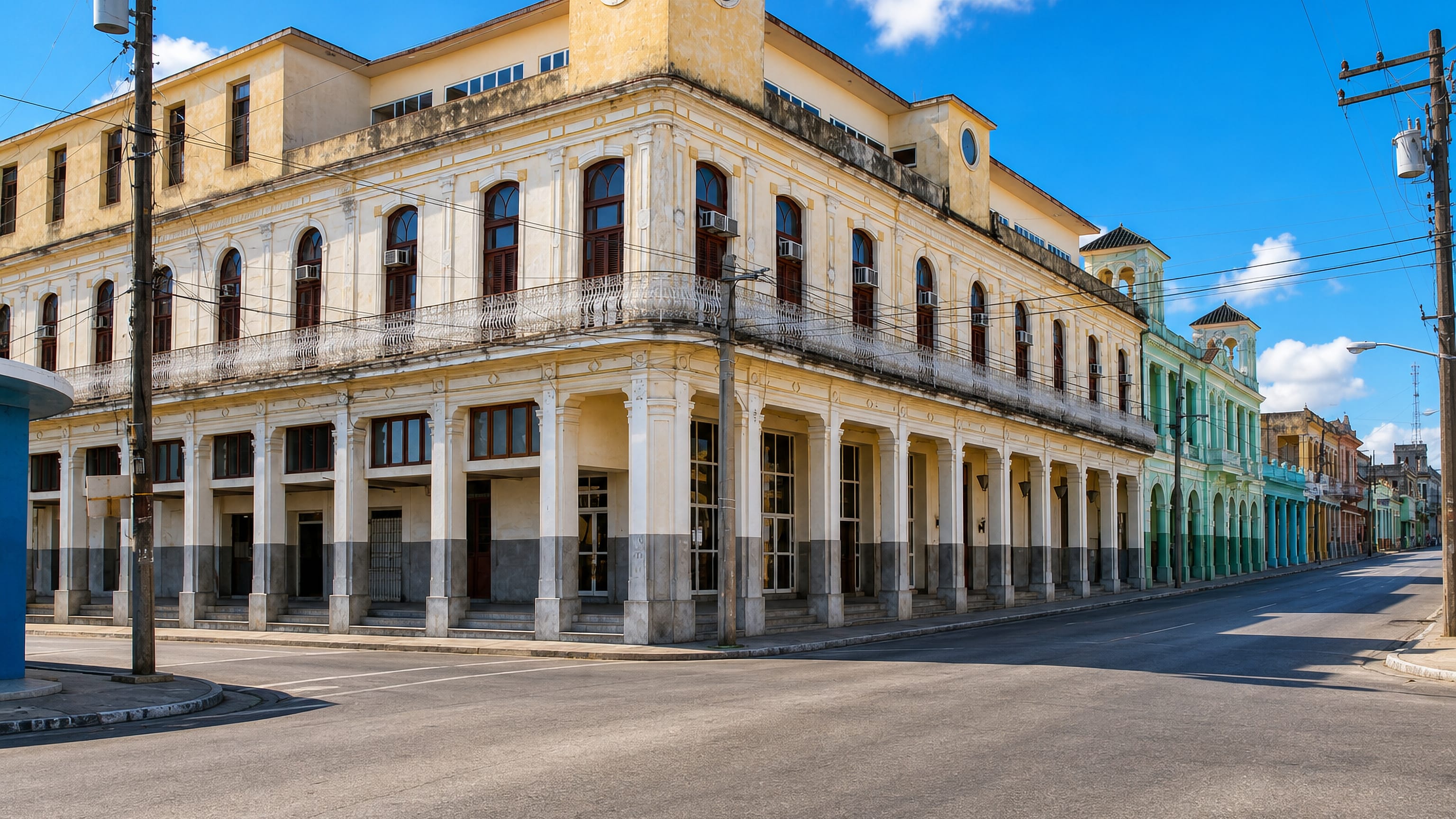 Yellow colonnaded corner building with a clock tower on an empty sunlit street in Pinar del Rio, Cuba.