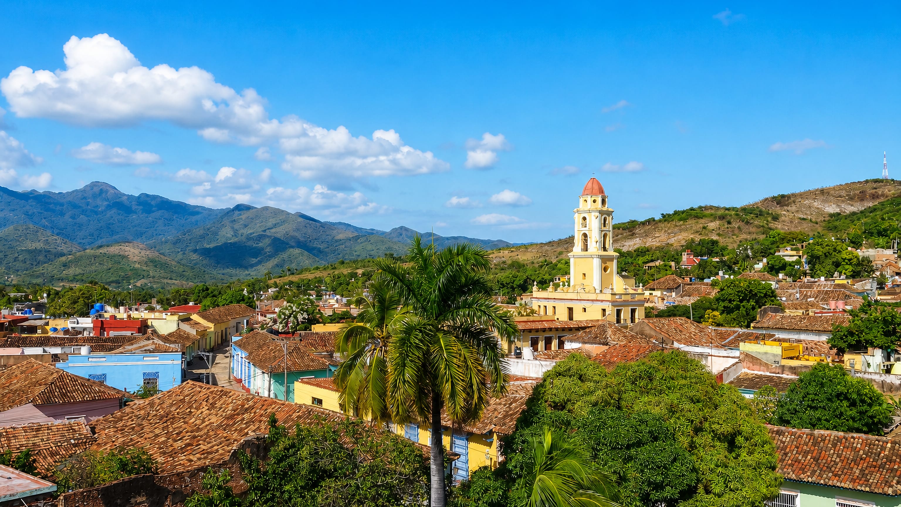 Terracotta rooftops of colonial Trinidad, Cuba, below a yellow bell tower with the Escambray mountains behind.