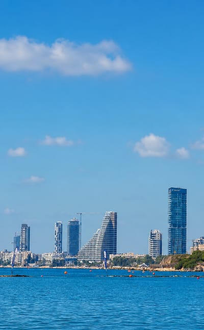 Limassol's modern seafront skyline of high-rise towers seen across the Mediterranean under a bright blue sky