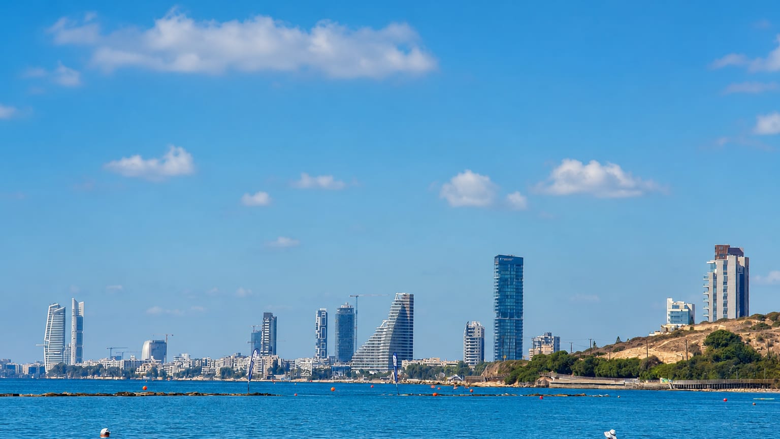 Limassol's modern seafront skyline of high-rise towers seen across the Mediterranean under a bright blue sky