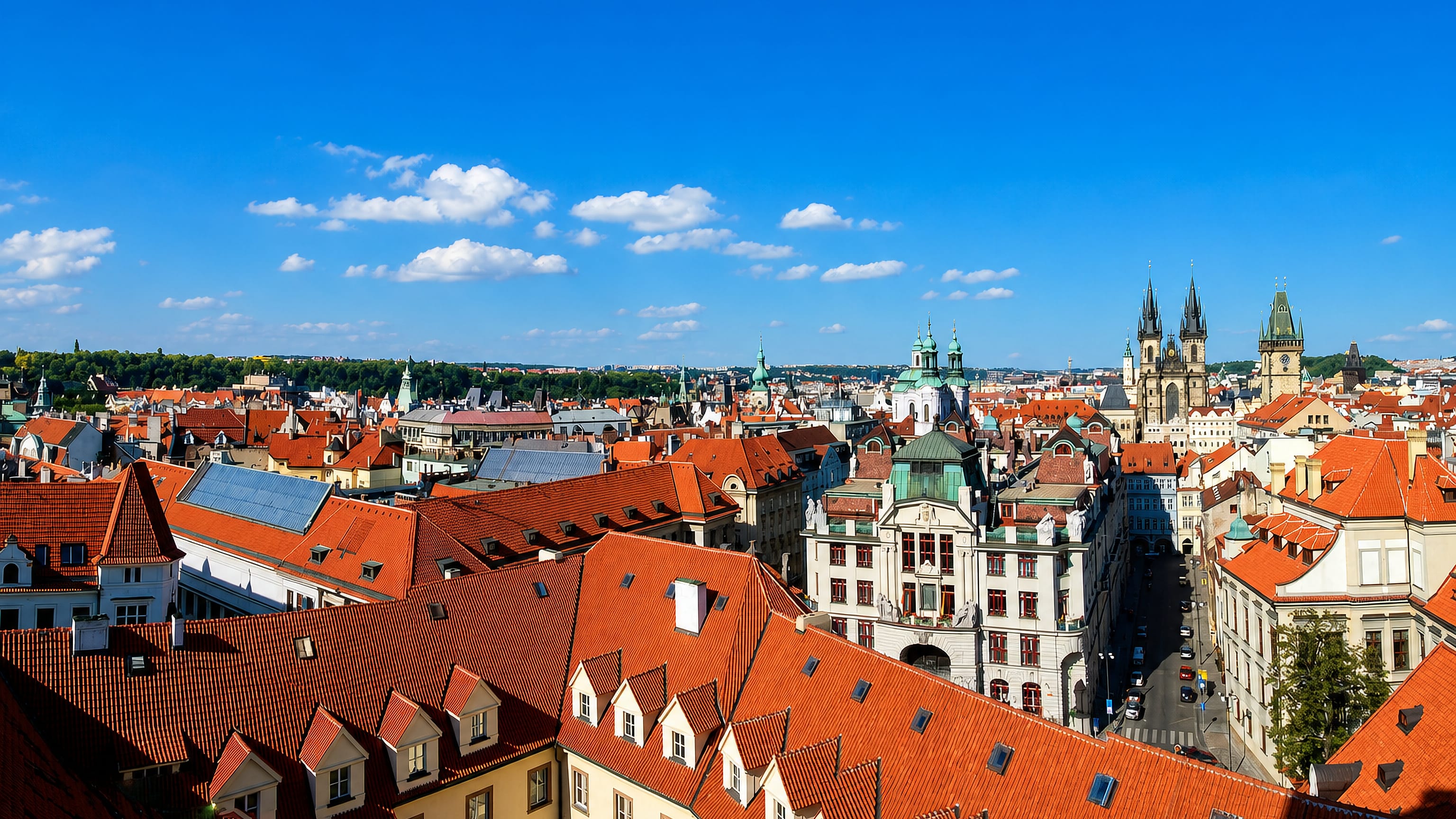 Red-tiled rooftops of Prague's Old Town with the Tyn Church spires and Old Town Hall tower.
