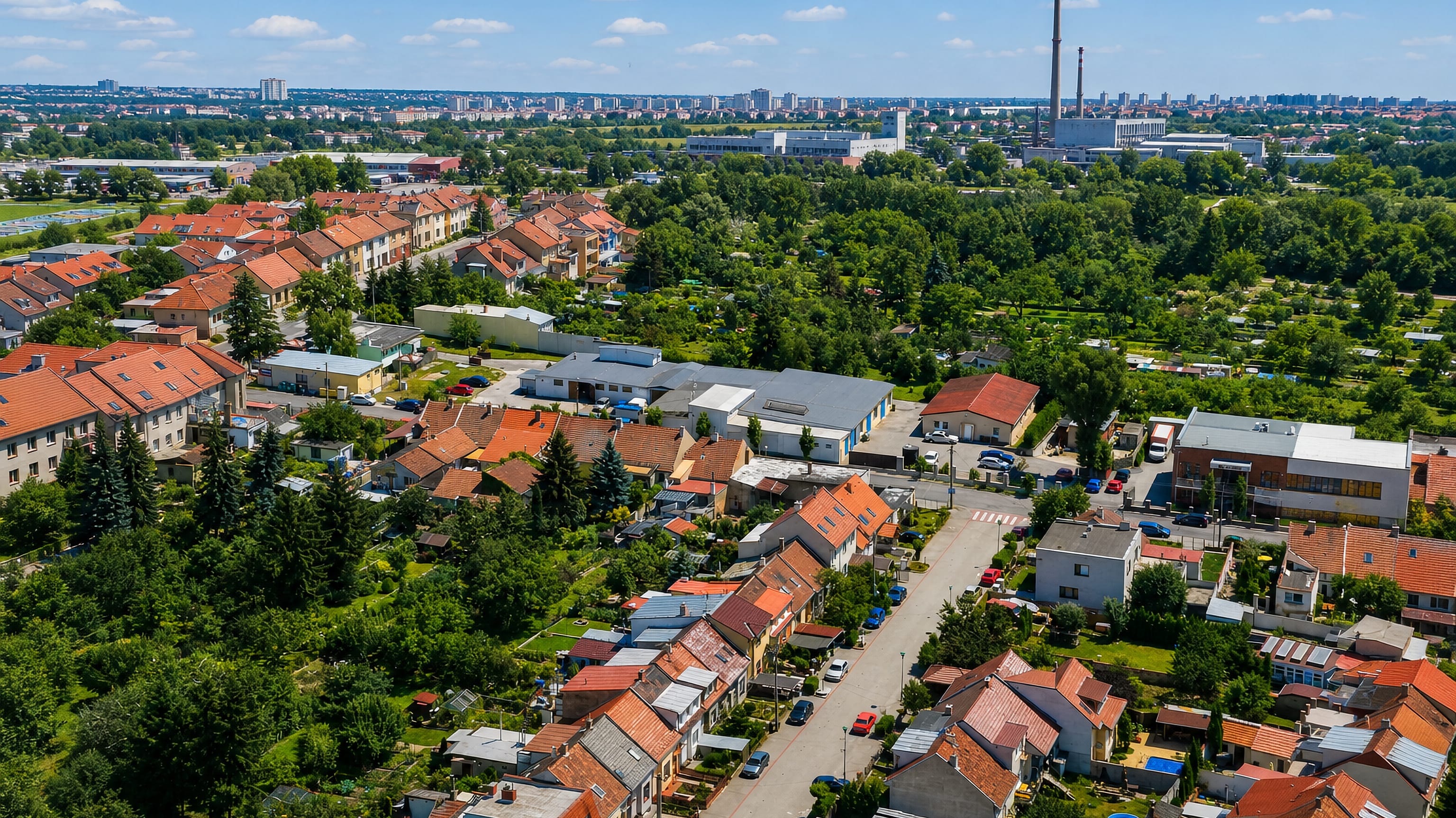 Aerial view of Brněnské Ivanovice, Brno, with red-tiled village houses, allotments and distant panel blocks.