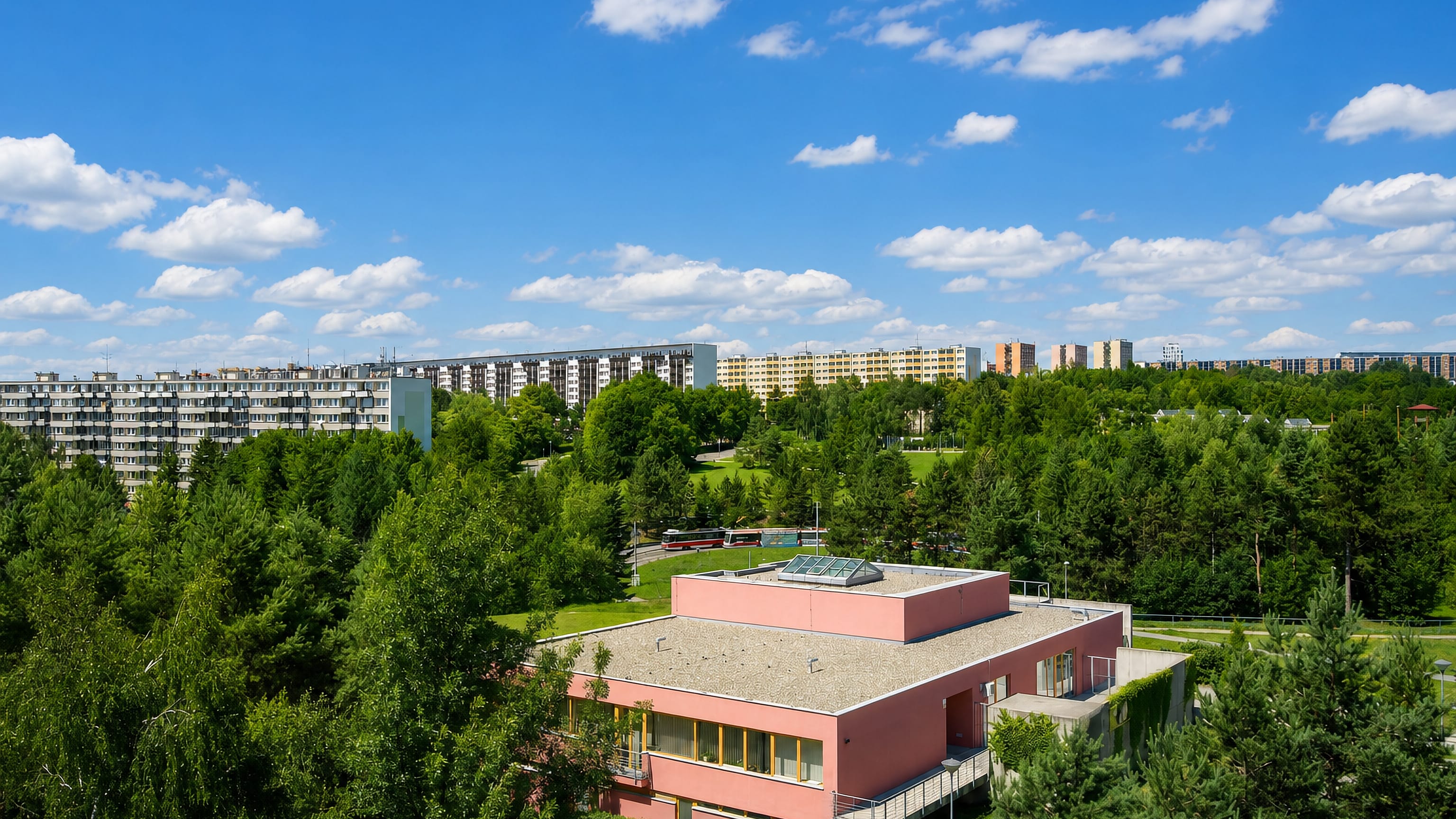 Aerial view over Lesná in Brno, with panel apartment blocks and a modern villa set among dense woodland.