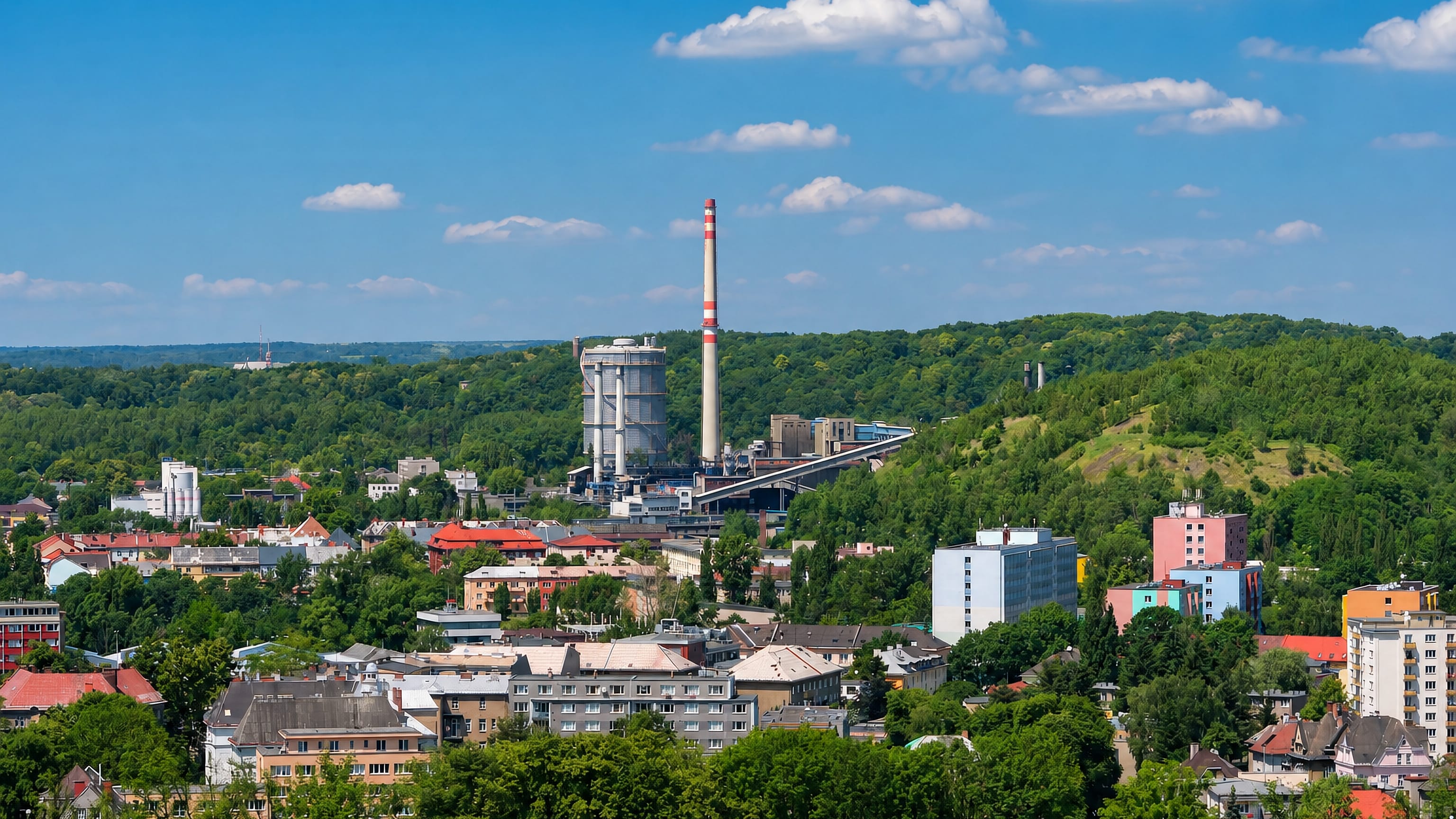 Industrial chimney and silo above wooded hills and mixed housing in Přívoz, Ostrava.