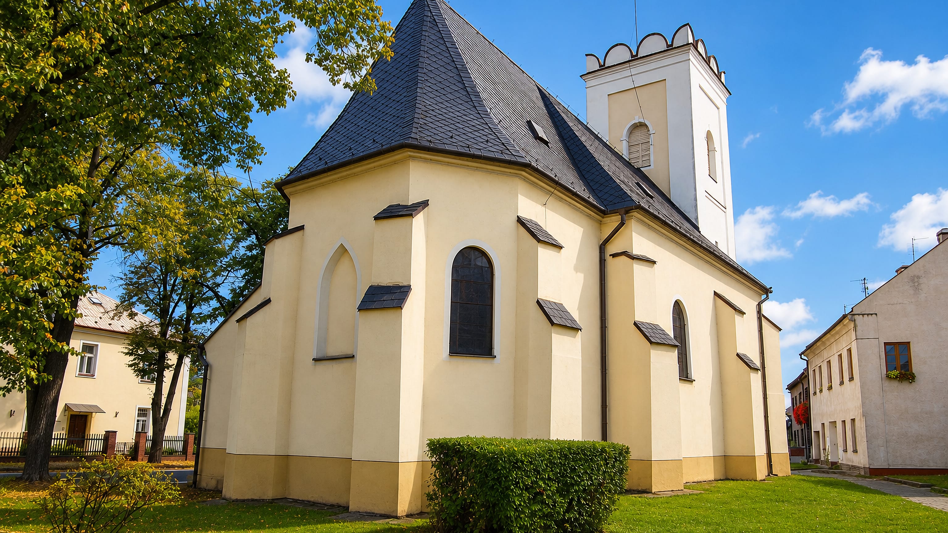 Pale yellow village church with white bell tower and slate roof in Chvalkovice, Olomouc.