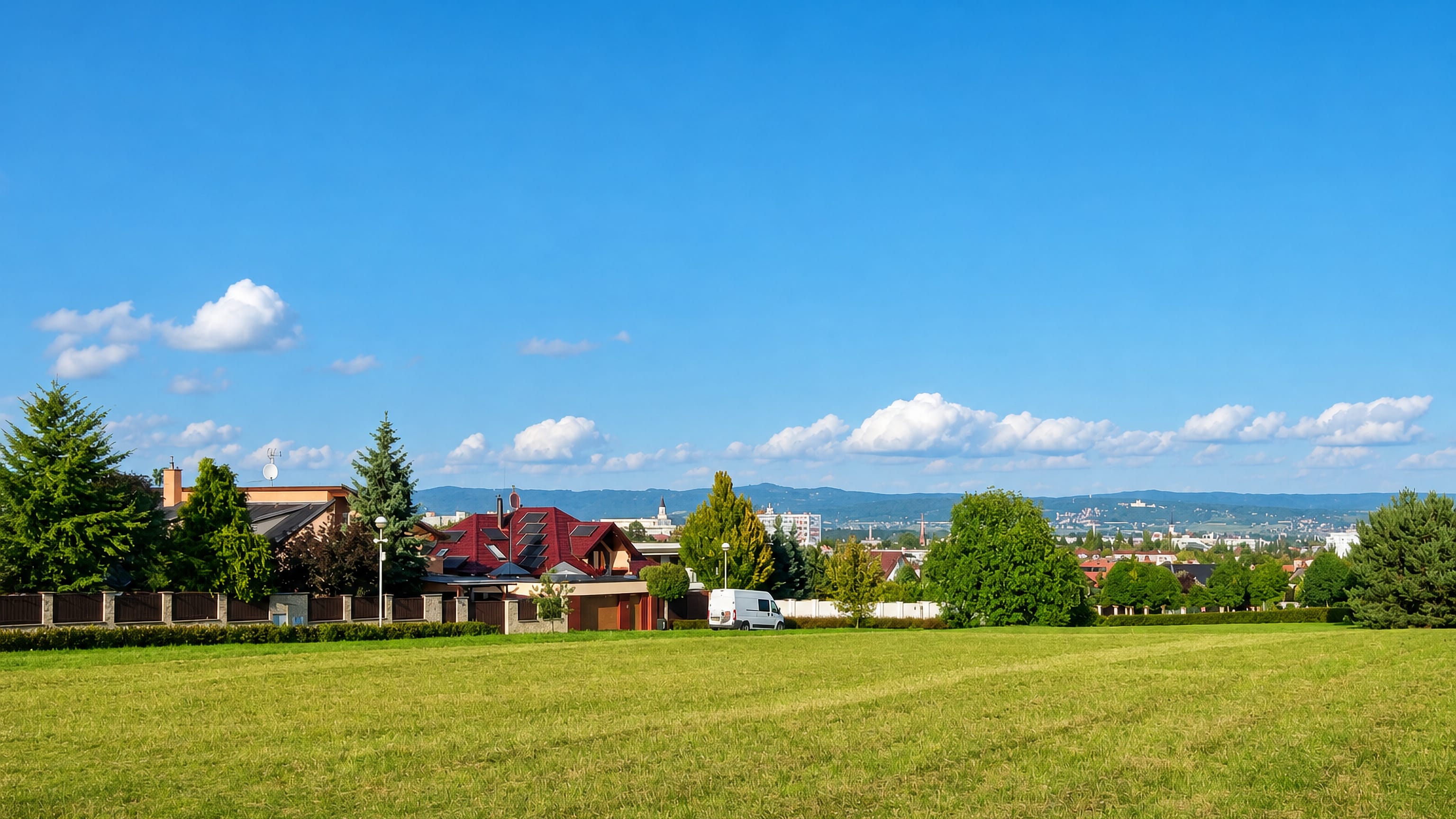Grassy meadow and red-roofed houses on Neredin's hillside above the Olomouc skyline and distant hills.