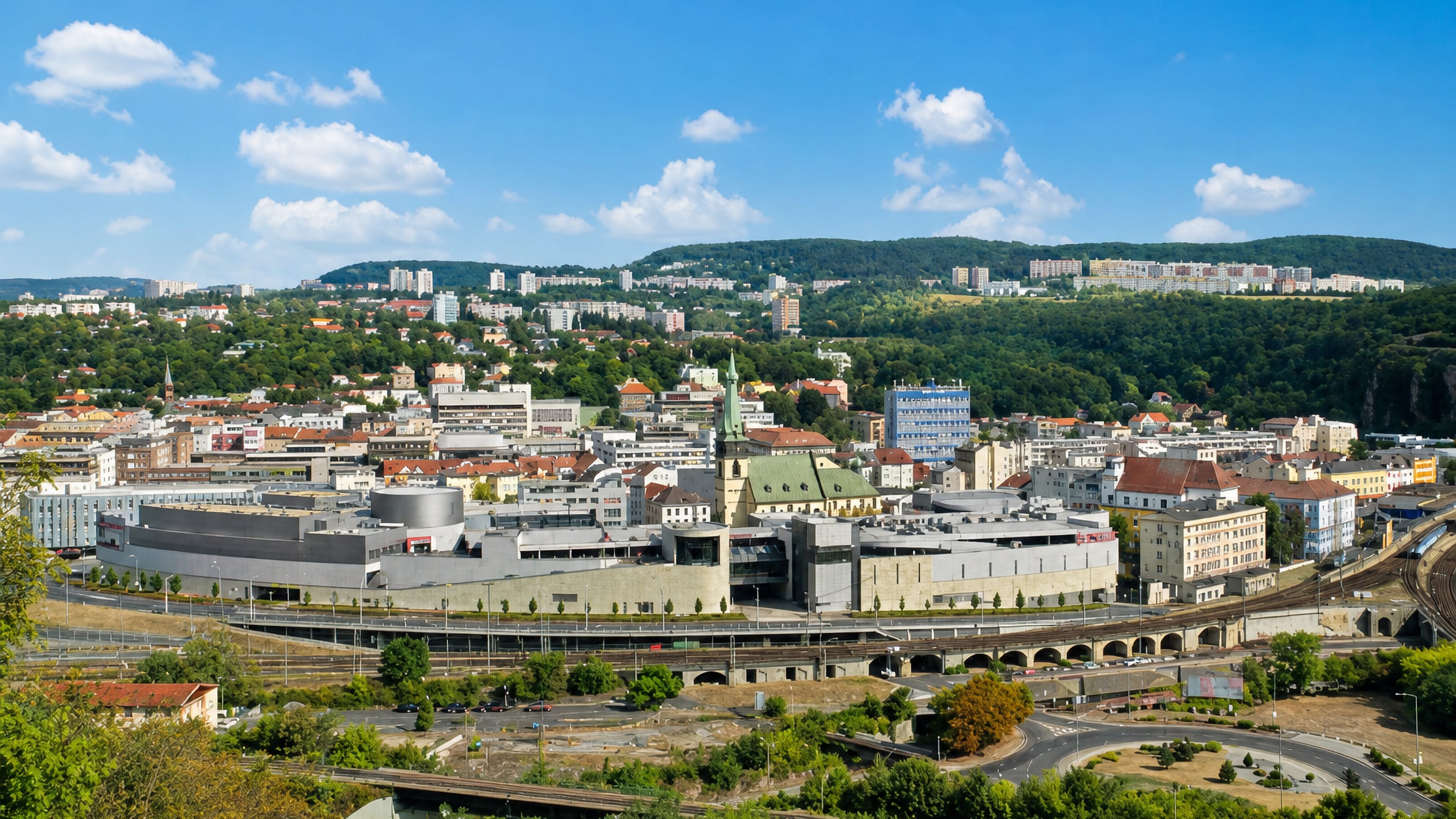 Ústí nad Labem from above, its green church spire, shopping centre and rail lines ringed by wooded hills.