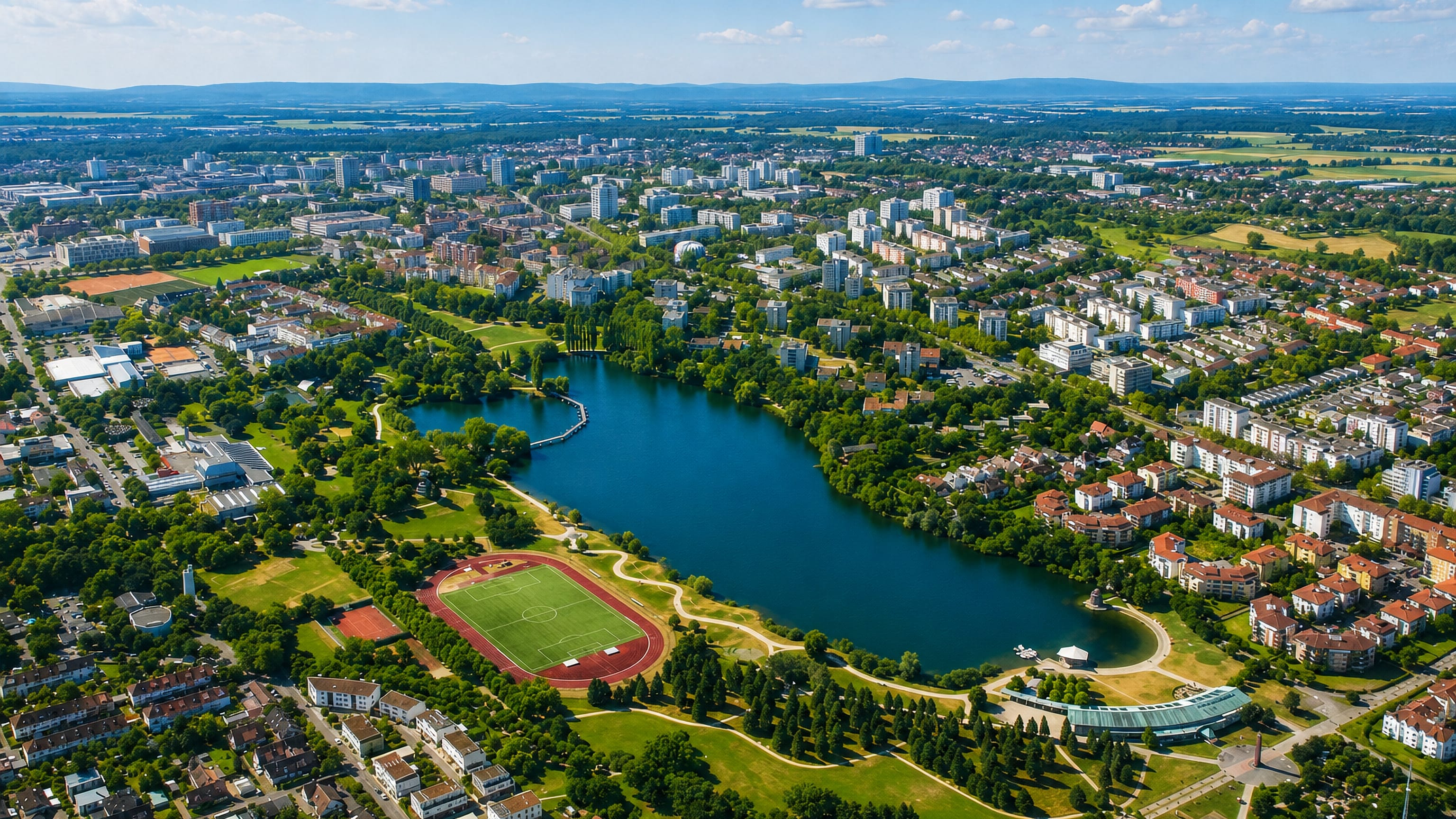 Aerial view of a lake, parkland and athletics track ringed by housing in Betzenhausen, Freiburg, Germany.