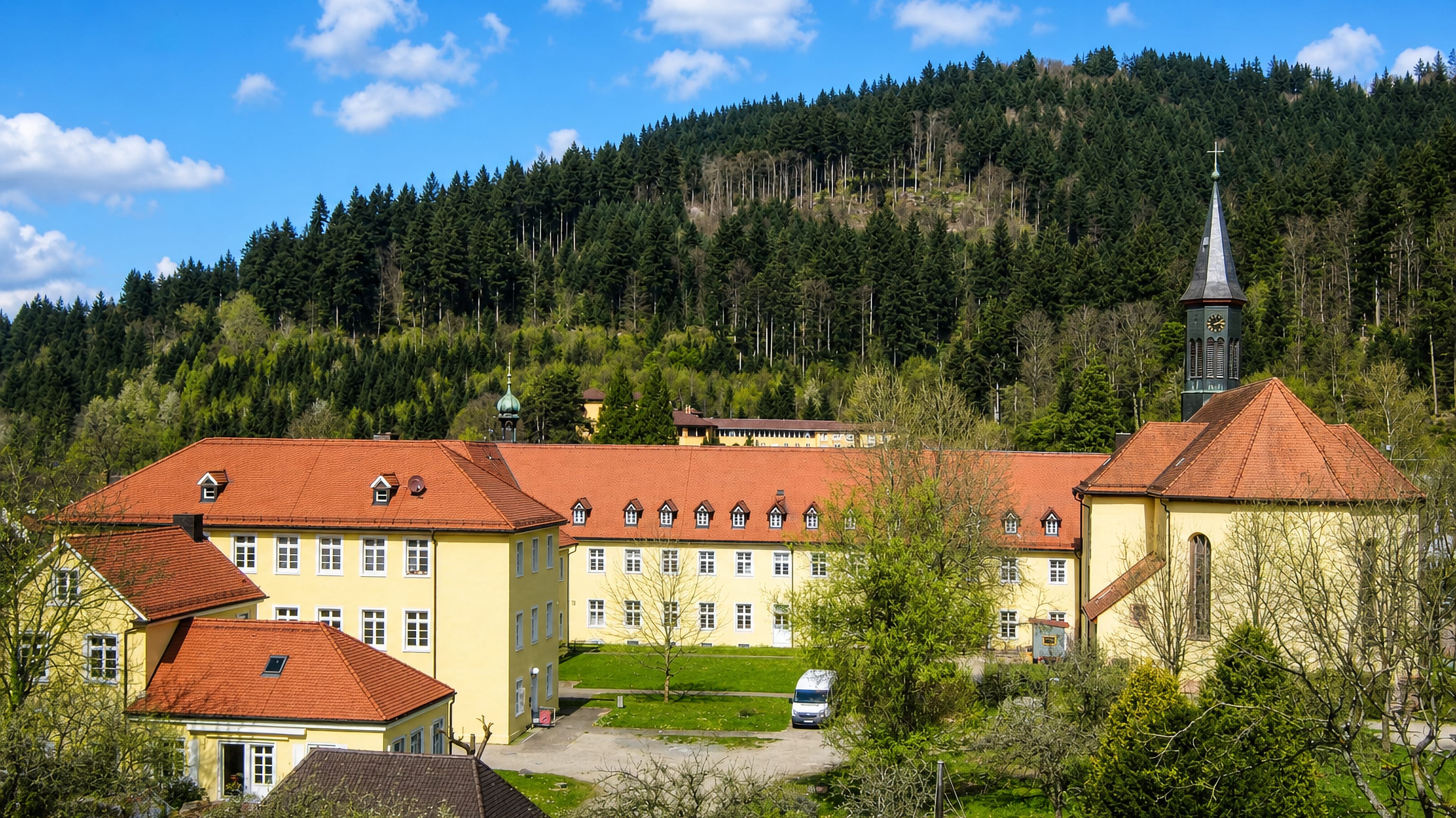The yellow former abbey buildings and church tower of Guenterstal, Freiburg, below forested Black Forest slopes.