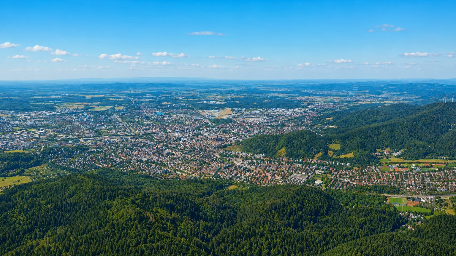 Distant aerial of Freiburg im Breisgau spread across its valley at the forested edge of the Black Forest.