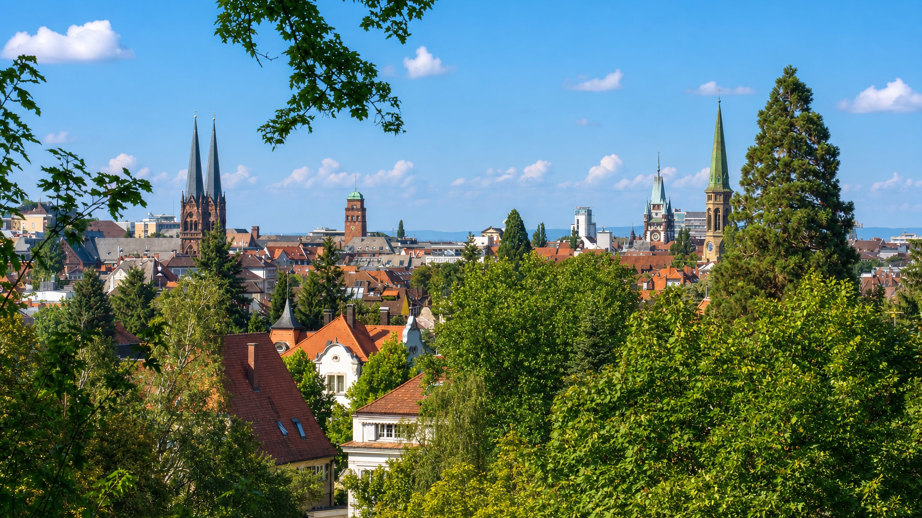 Freiburg's Wiehre district seen over treetops, with church spires and the Münster tower on the skyline.