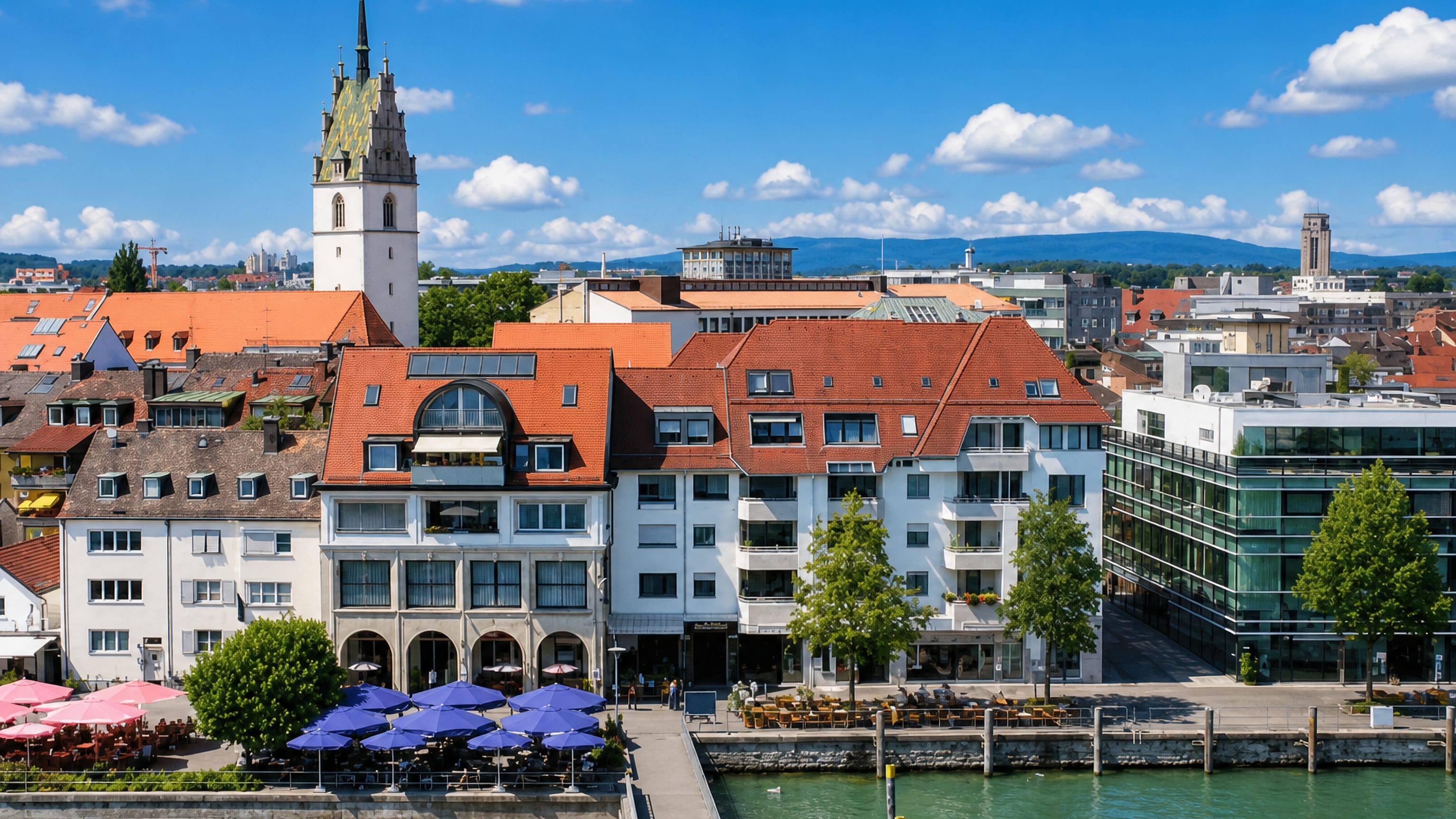 Friedrichshafen's Lake Constance waterfront with promenade cafes and the tiled spire of St Nikolaus church.